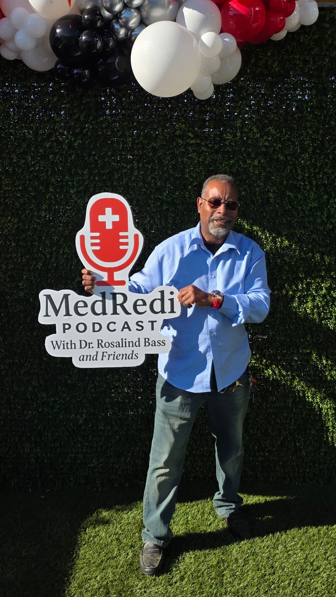 Guest posing with MedRedi Podcast sign at branded photo wall with balloon arch